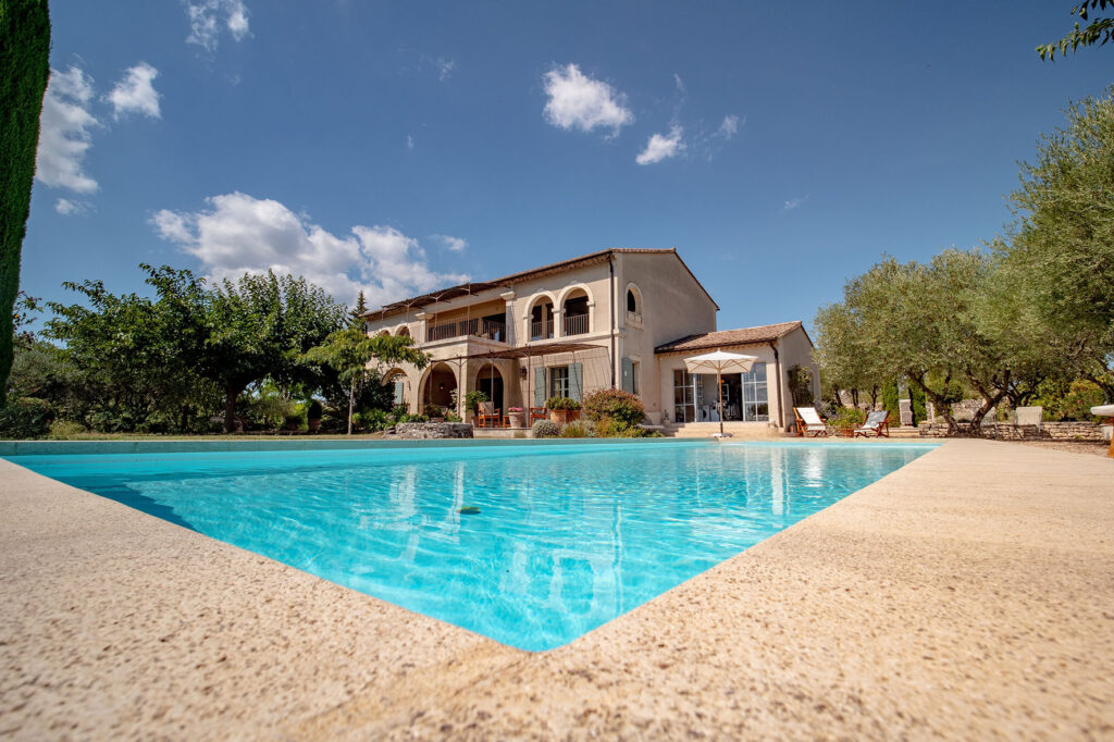Uzes, France - August the 31st 2021 : provencal villa in the south of france with the pool in the foreground, olive trees, arches, lounge chairs and sunny weather, blue sky